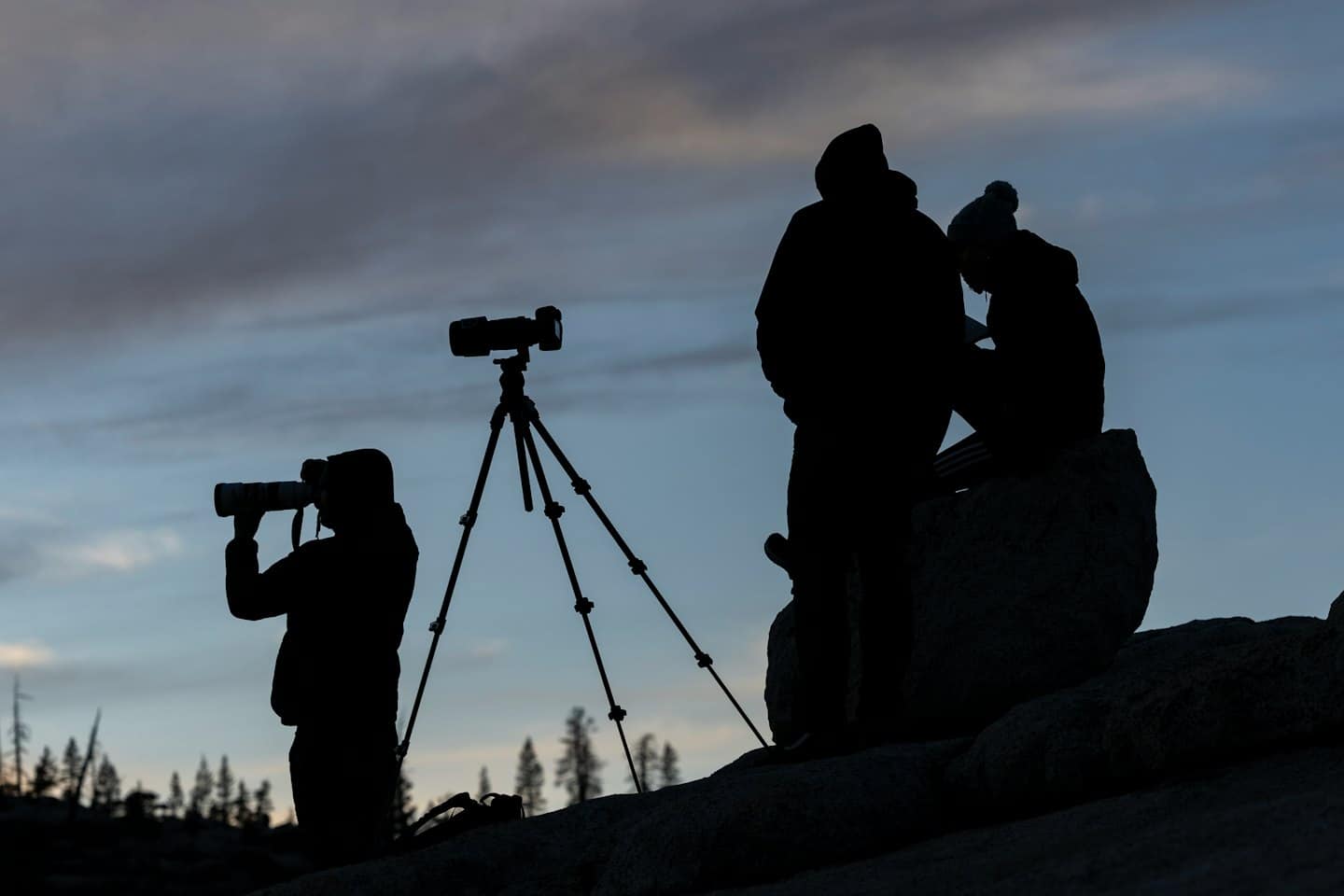 Cztery osoby zbierają się na skalistym wzgórzu, aby sfotografować zachód słońca.
